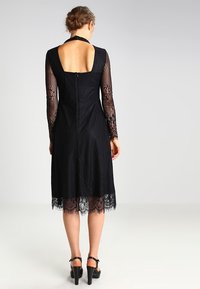 Černé šaty s dlouhými krajkovými rukávy, ribbovanou texturou, nízkým výstřihem na zádech a krajkovým lemem. Zapínání na zip vzadu. Elegantní design.