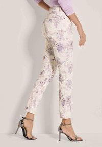 Creme kleurige broek met een bloemenpatroon in paarse tinten, slim fit, hoge taille, met achterzakken en gecombineerd met metallic hoge hakken.