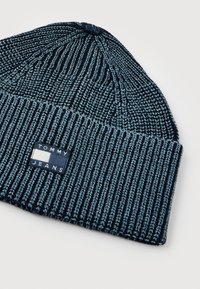 Tume sinise ribaga kudumüts, millel on volditud äär ja ees on valge, tumesinine ja punane ristkülikukujuline "Tommy Jeans" logo silt.