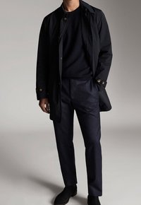 Navy jacket with gold buttons, navy textured sweater, and dark trousers. The outfit features a streamlined design and smooth fabric textures.