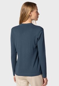 Pitkähiuksinen tummansininen neule, jossa on pyöreä kaula-aukko, ribatut hihansuut ja helma. Sileä pinta ja vartalonmyötäinen leikkaus.