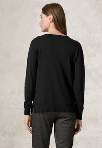 Maglione nero a maglia con maniche lunghe, polsini e orlo a coste, aperture laterali e scollo rotondo, abbinato a pantaloni con motivo a spina di pesce.