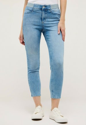 Light blue cropped skinny jeans with elastic waistband and front pockets, worn with white sneakers on a plain background.