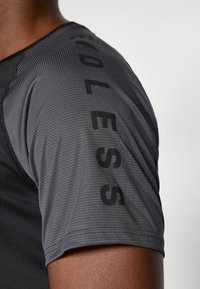 T-shirt de sport gris avec un tissu texturé, des manches courtes et un impression audacieuse du mot "INFINI" le long de la couture de l'épaule.