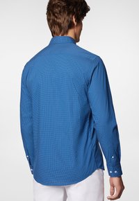 Niebieska koszula z długim rękawem, z wzorzystą teksturą i prostym wykończeniem dołu. Posiada guziki na mankietach oraz klasyczny krój kołnierzyka.