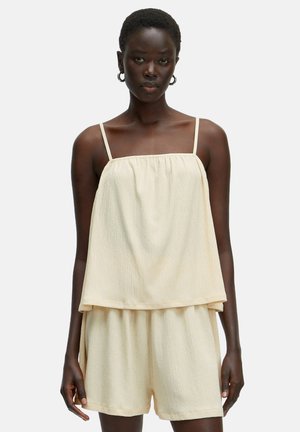 Light yellow two-piece set featuring a loose, gathered top with thin straps and matching shorts with an elastic waistband. Textured fabric.