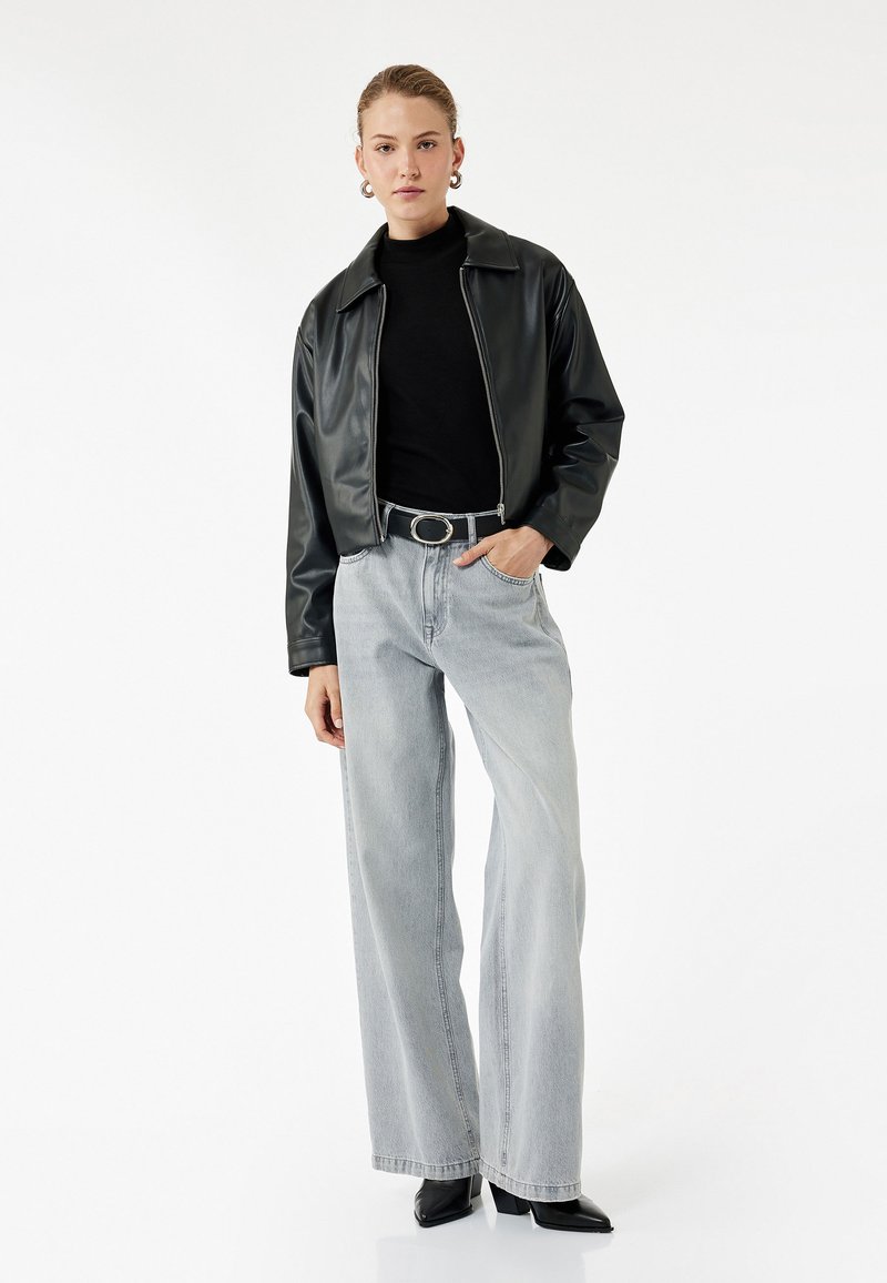 Chaqueta de cuero sintético negra con un collar plano, combinada con pantalones vaqueros de tiro alto en azul claro y de pierna ancha, y botas negras de punta.