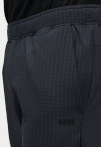 Κοντινή λήψη μαύρου υφασμάτινου παντελονιού με πλαϊνές τσέπες και το λογότυπο "BOSS" ανάγλυφο κοντά στην τσέπη στο δεξί πόδι.