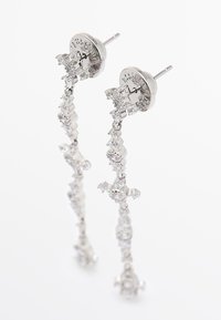 Orecchini pendenti in tonalità argento con strass trasparenti disposti a forma di croce, dotati di perni a lobo e chiusure a farfalla su sfondo bianco.