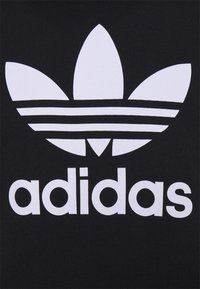 Adidas-logotyp med tre vita trefolblad och tre horisontella ränder ovanför den lilla texten "adidas" på en svart bakgrund.