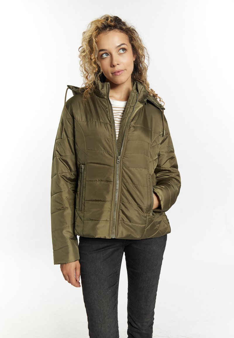 Giacca piumino verde oliva con chiusura con zip, design trapuntato, cappuccio e due tasche frontali; abbinata a una maglietta a righe e pantaloni scuri.