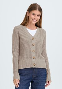 Beige knitted cardigan with a V-neck, featuring five wooden buttons down the front, ribbed cuffs, and a fitted hem. Worn over a white shirt.