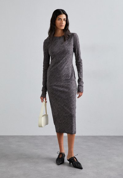 Long-sleeve, fitted dress in dark gray ribbed fabric; knee-length with side slits. Paired with a white, curved handbag and black, gathered shoes.