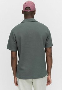 Kortärmad, strukturerad grön skjorta med krage; bärs med en rosa keps. Funktioner inkluderar en avslappnad passform och rena sömsdetaljer.