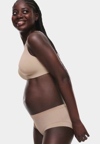 Reggiseno senza cuciture e slip coordinati su un modello, realizzati in tessuto morbido con una vestibilità comoda, che mostrano un design semplice e un colore neutro.