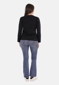 Maglione nero a maniche lunghe con scollatura rotonda, abbinato a jeans chiari svasati e sneakers bianche con accenti neri.
