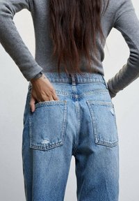 Jean en denim bleu clair avec une taille haute, deux poches arrière, une légère usure et une coupe droite, associé à un haut gris ajusté.