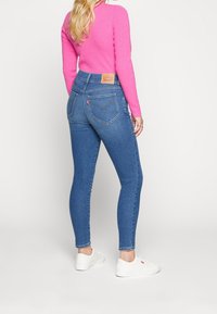 Jeans ajustados de mezclilla azul con una cintura alta y costuras visibles, combinados con un suéter ajustado de color rosa brillante y zapatillas blancas.