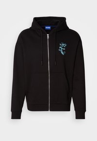 Sweat à capuche zippé noir avec poches avant, capuche à cordon, et petit motif de fleur bleue sur la poitrine gauche, étiqueté "HUGO" à l'intérieur du col.