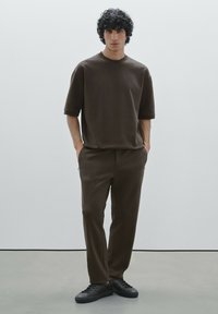 Braunes, kurzärmeliges, übergroßes T-Shirt kombiniert mit passenden Hosen; strukturierter Stoff; minimalistisches Design; ergänzt durch schwarze Sneaker.