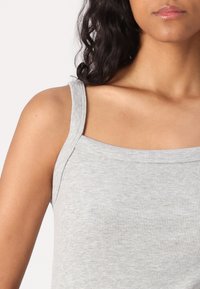 Top in cotone grigio a costine con spalline larghe e scollatura a girocollo. Texture morbida, design aderente che mette in evidenza la elasticità e il motivo del tessuto.