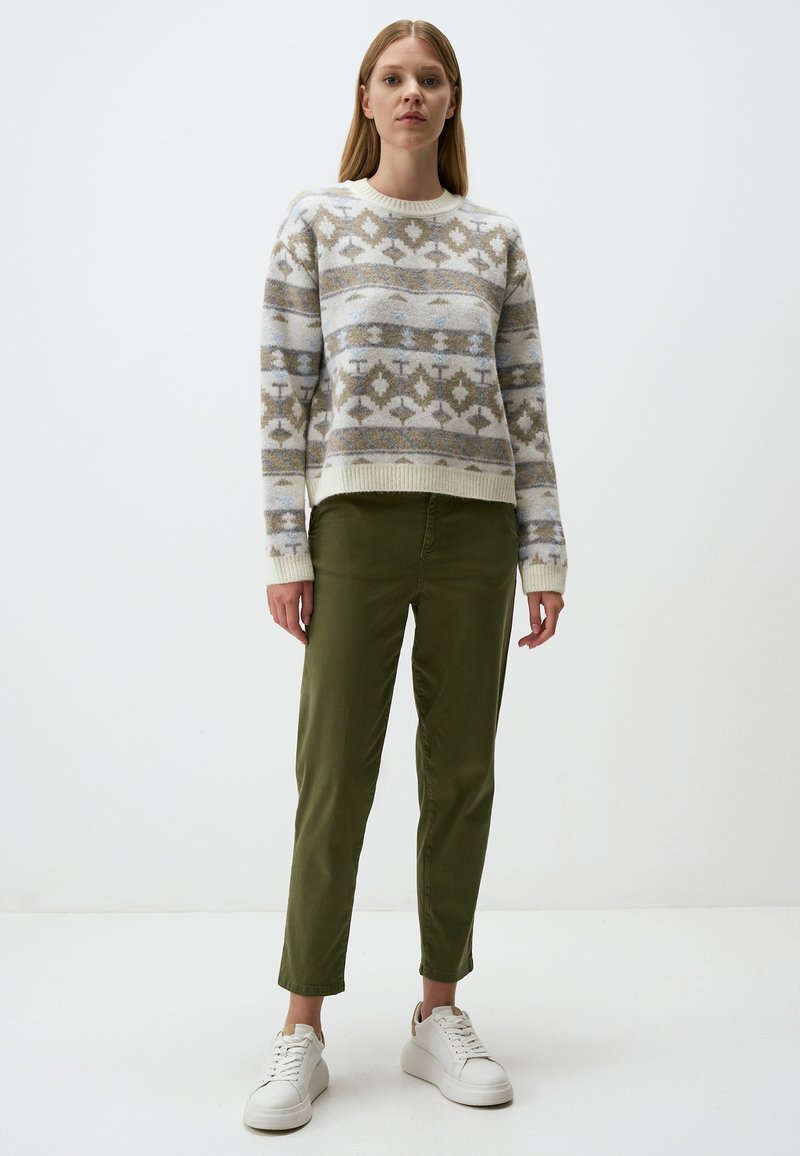 Maglione lavorato a maglia con motivi geometrici in beige e azzurro chiaro, abbinato a pantaloni verde oliva a sigaretta e sneakers bianche.