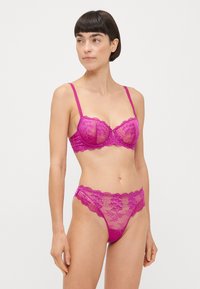 Ensemble de lingerie en dentelle de fuchsia vif. Soutien-gorge balconnet avec des motifs floraux complexes et des bords festonnés ; string assorti avec des détails similaires.