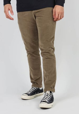 Pantalons en velours côtelé beige avec une coupe slim et une texture subtile, associés à des baskets en toile noires avec des accents et des lacets blancs.