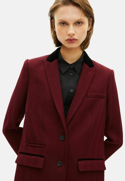 Blazer bordeaux con motivo a spina di pesce, colletto in velluto nero, due tasche frontali e chiusura con bottone, indossato sopra una camicia nera.