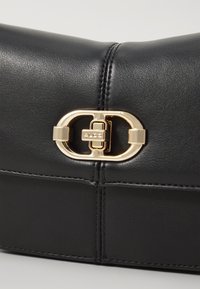 Črna usnjena torbica s strukturirano obliko, z zlatim mehanizmom in vidnimi šivi ob robovih.