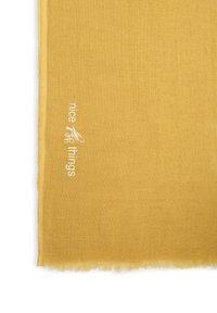 Écharpe en lin jaune moutarde aux bords effilochés. Présente un texte brodé "nice things" en blanc avec un motif d'accent. Texture douce et légère.