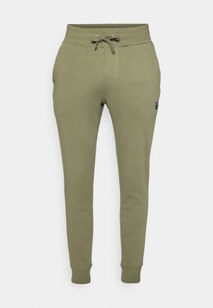 Green cotton blend joggers featuring an elastic waistband with a drawstring, side pockets, and ribbed cuffs. Small logo patch on the side.