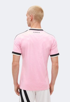 Person med kort blondt hår iført en lyserød Juventus sportstrøje med sort og hvid kant, set bagfra.