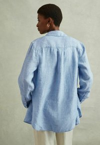 Camicia azzurra chiara a maniche lunghe in lino con colletto e polsini con bottone, caratterizzata da un fit rilassato e dettagli con piega sul retro.