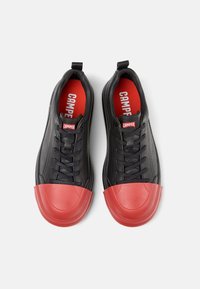 Schwarze Ledersneaker mit roten Gummispitzen und Schnürsenkeln. Merkmale eine rote Innensohle mit "CAMper"-Markierung. Glatte Textur, niedrig geschnittenes Design.