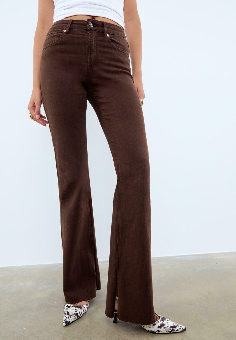 Jeans marron évasés à taille haute, avec une fermeture à bouton sur le devant. Associés à des talons aiguilles à motif noir et blanc.