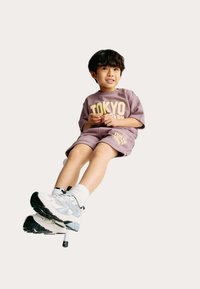 Pantalones cortos morados y camiseta extragrande a juego con el texto "TOKYO", combinados con zapatillas blancas con detalles azules y suelas negras.