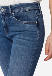 Jeans de mezclilla azul oscuro con un corte ajustado, diseño clásico de cinco bolsillos y costuras en contraste. Presenta una pequeña etiqueta de la marca en la cinturilla.