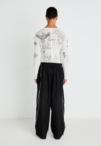 Long-sleeve, white top with black artistic prints; paired with loose, black pants featuring white side stripes and an elastic waistband.