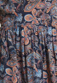Tissu bleu foncé avec motif cachemire complexe dans des nuances d'orange, bleu clair et crème, présentant des plis froncés.