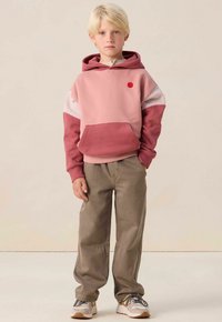 Sweat-shirt à capuche rose et marron avec une poche avant et un point d'accent rouge ; associé à un pantalon beige ample et des baskets grises.