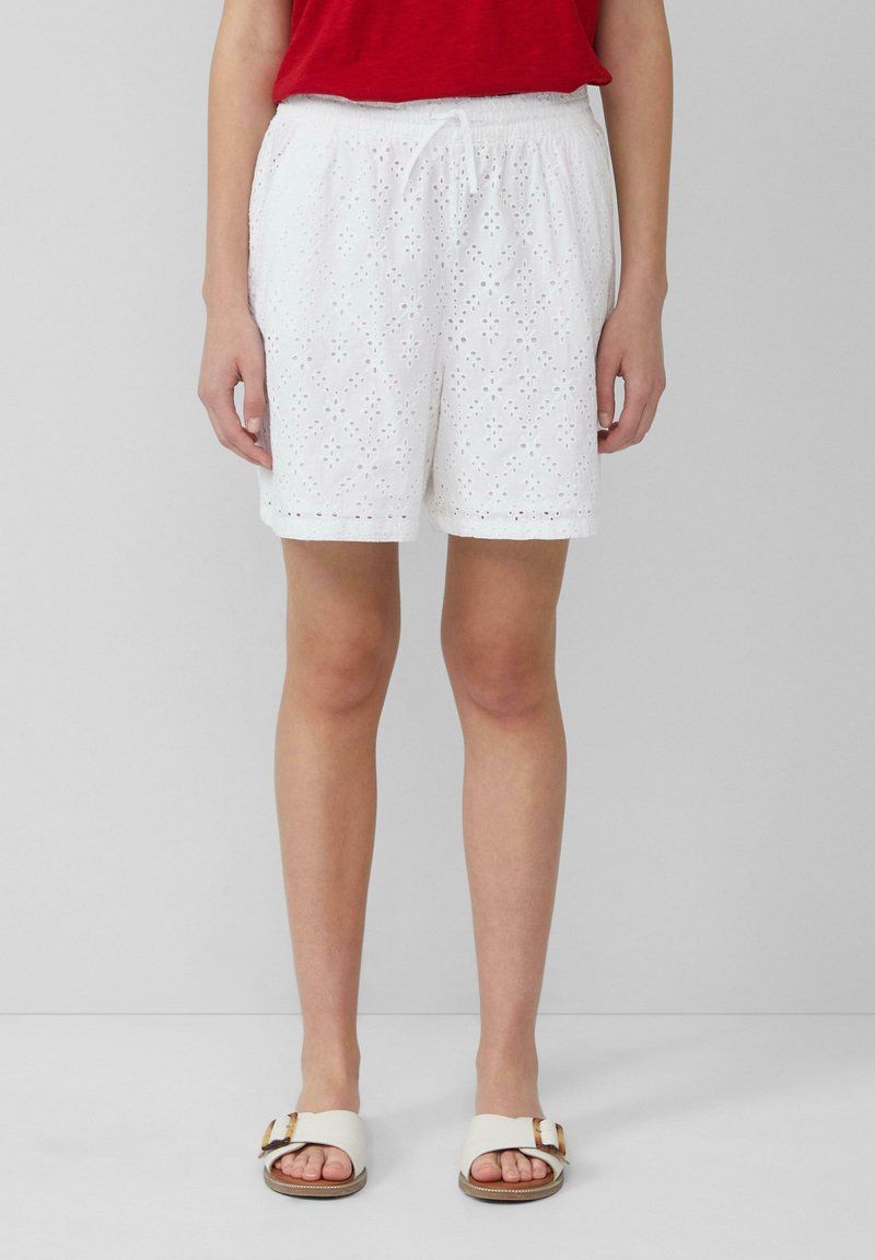 Witte shorts met geborduurde bloemenuitsparingen, voorzien van een elastische tailleband en koord. Gecombineerd met beige sandalen.