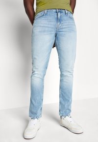 Jeans in denim blu chiaro con una vestibilità slim, caratterizzati da un classico design a cinque tasche e un leggero effetto sbiadito. Abbinati a sneakers bianche.