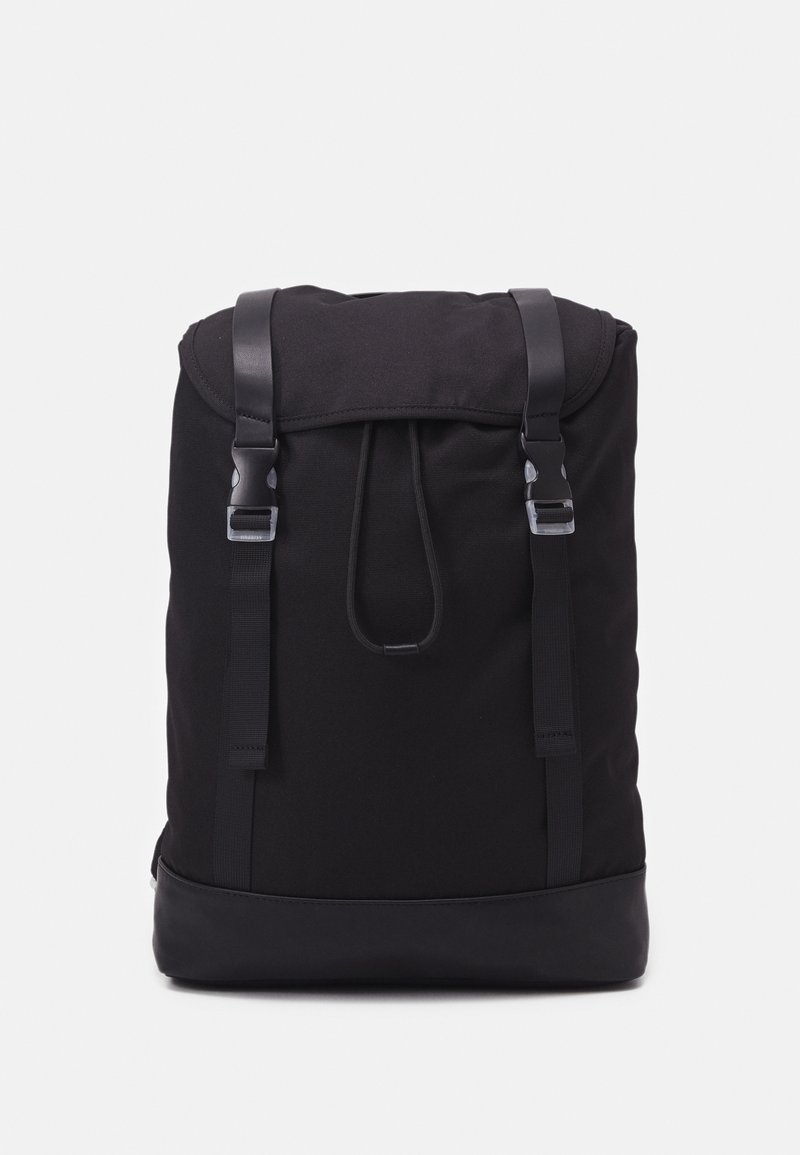 Sac à dos en tissu noir avec rabat supérieur sécurisé par deux sangles noires et boucles argentées, et une base noire renforcée.