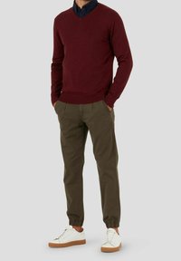 Bordeauxfarbener Pullover mit V-Ausschnitt, kombiniert mit olivgrünen Jogginghosen und weißen Sneakern mit braunen Sohlen. Slim Fit, gerippte Bündchen und Bund.