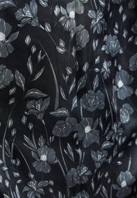 Sort stof har et blomsterprint i grå nuancer, der viser detaljerede blomster og blade med en glat tekstur.