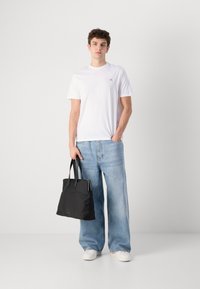 Camiseta blanca de manga corta, jeans de pierna ancha en azul claro y bolso tote negro con asas negras, combinados con zapatillas blancas.