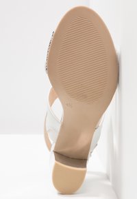 Semelle d'une sandale à talon blanche avec un dessous en caoutchouc beige texturé et la taille 4½ marquée près de la voûte plantaire.