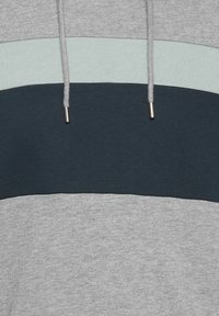 Tissu de sweat à capuche avec trois blocs de couleur horizontaux en gris, bleu clair et bleu foncé, doté de cordons gris à embouts métalliques.