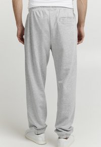 Grå joggebukser med elastisk midjebånd, sidelommer og avsmalnende mansjetter. Laget av et mykt stoff med en glatt tekstur.